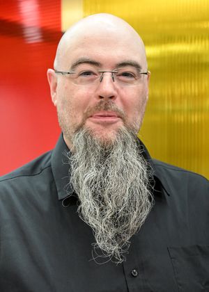 Wes Dean wearing a black shirt in front of a red and yellow background